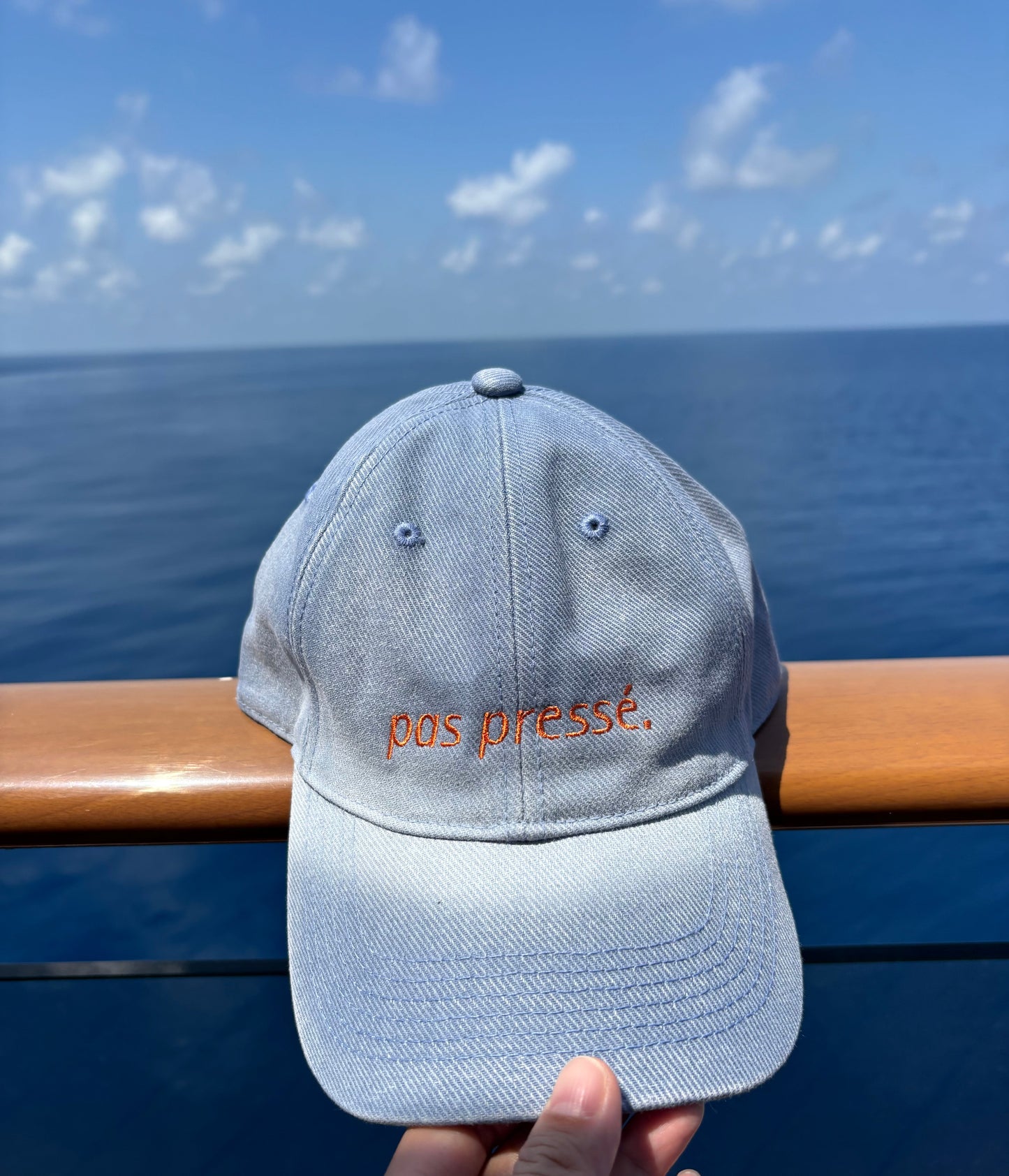 Gray cap with 'post press' embroidery held by a hand against a blue sky background
