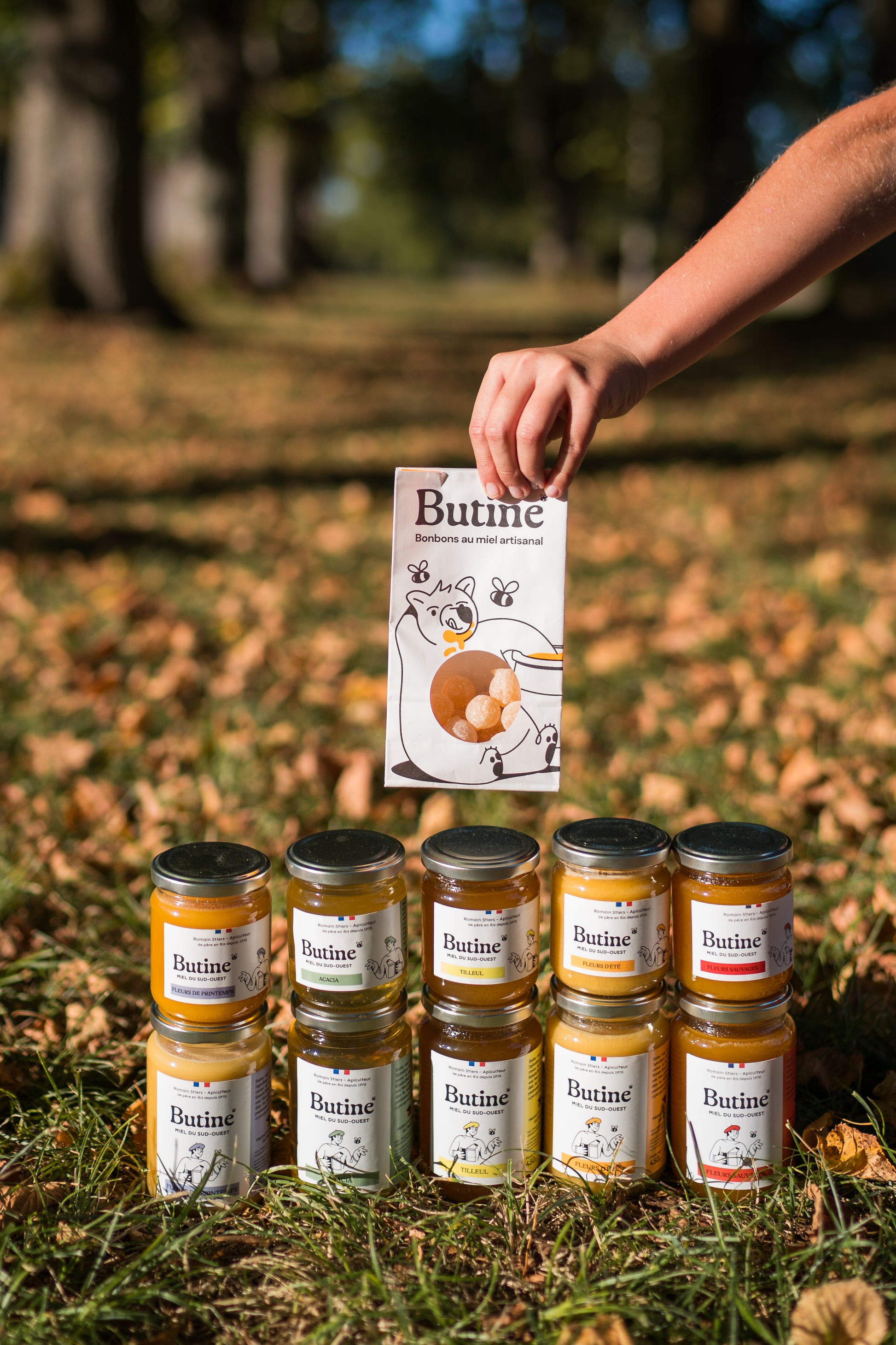 Jars of 'Butine' honey with a person holding a product card in an outdoor setting.