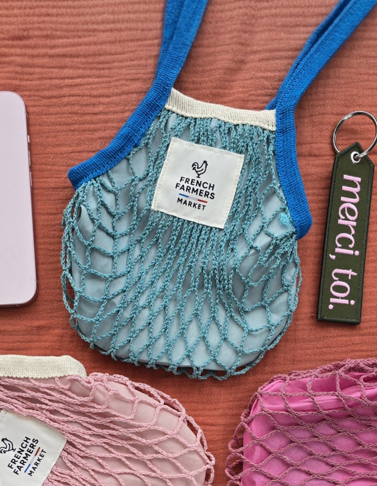 Mesh produce bags in various colors with tags on a red surface, alongside a phone and pen.