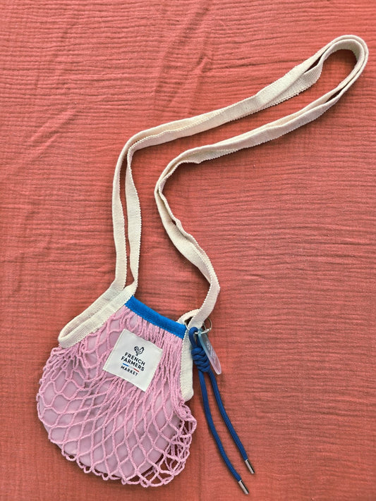 Pink mesh bag with a strap on a textured red surface