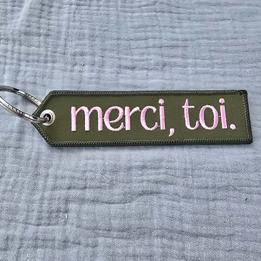 Keychain with 'merci, toi.' text on a textured gray background