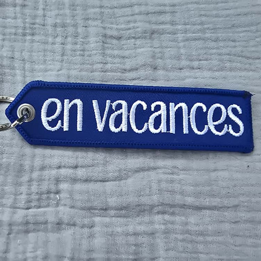 Blue keychain with 'en vacances' text on a textured gray background