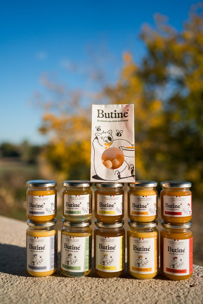 Jars of Butine honey stacked with a box on a natural background