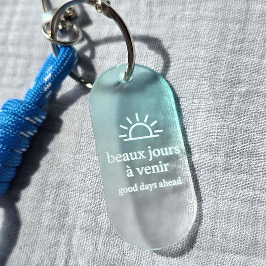 Glass keychain with 'beaux jours à venir' text on a gray background