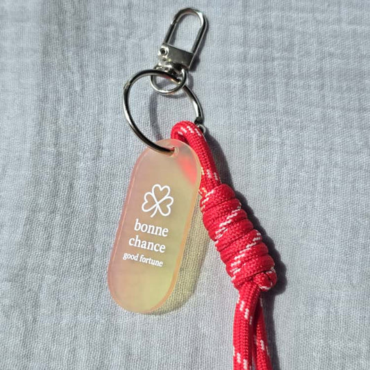 Keychain with red cord and 'bonne chance' tag on a gray background