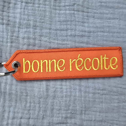 Orange keychain with 'bonne reçolte' text on a gray fabric background