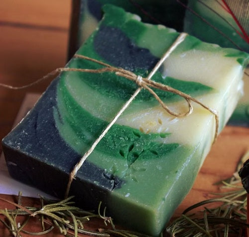 Three-layered soap bar with green, white, and blue layers tied with twine on a wooden surface.
