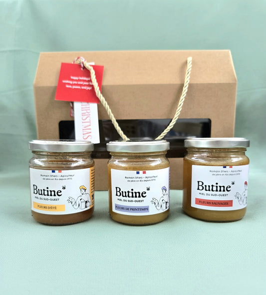 Three jars of 'Butine' spread on a light green surface with a cardboard box in the background.